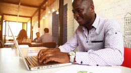 Young black, well-dressed man working on job application on his laptop in a trendy cafe