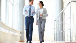 Business woman and man walking down the hall of a corporate office building and having a discussion