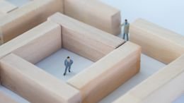 2 businessmen figurines in a maze made out of wooden blocks trying to work around their problems