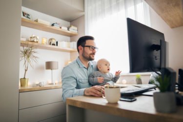 A man works remotely while holding his baby 